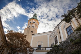 A striking tower stands out against a cloudy sky, next to it an autumn-coloured tree, Mikulov