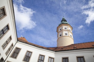 A historic tower rises under a clear blue sky, surrounded by buildings with red tiled roofs,