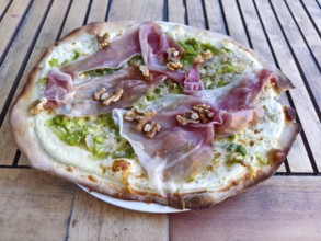 Close-up of a pizza tarte flambée with raw ham and walnuts, crispy base, served to a high standard,