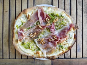 A gourmet pizza tarte flambée with raw ham and walnuts served on a wooden board, Lower Austria