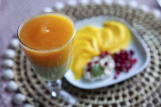 A glass with multi-coloured juice and a plate with mango slices and pomegranate seeds, Lower