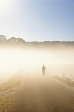 Person in silhouette running on a dirt road in autumn fog in the countryside