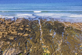 Beach by the sea at low tide with water pools and waves crashing on the shoreline a sunny summer