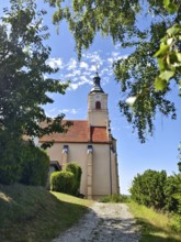 Church in the countryside with a tower on a sunny summer day, surrounded by trees and a path,