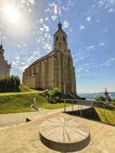 Baroque church in the sunshine with an impressive tower, surrounded by green landscape and blue