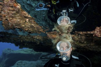 Diver with open blonde hair reflected in large air bubble in cave ceiling in underwater grotto,