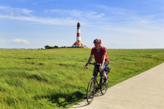 Cyclist, cycle tour through salt marshes, Westerheversand lighthouse on the horizon, Cirrus,