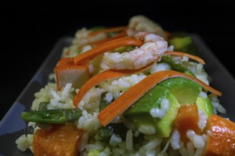 Rice salad with shrimp, red bell pepper and avocado, on black background