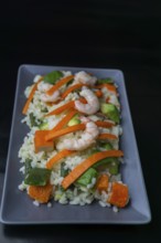 Rice salad with shrimp, red bell pepper and avocado, on black background