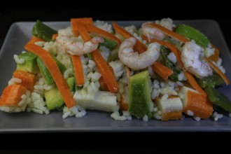 Rice salad with shrimp, red bell pepper and avocado, on black background