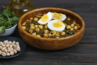 Wooden bowl with chickpeas with spinach and hard-boiled egg on wooden table