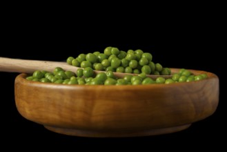 Wooden bowl with fresh peas and wooden spoon isolated on black background