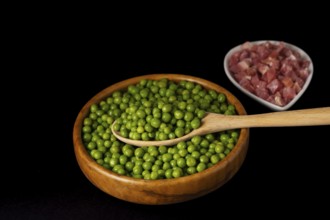 Wooden bowl with peas and white bowl with iberian ham isolated on black background