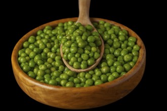 Wooden bowl with fresh peas and wooden spoon isolated on black background