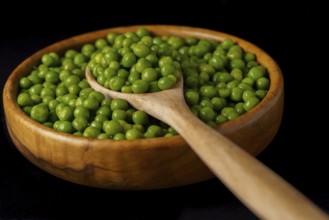 Wooden bowl with fresh peas and wooden spoon isolated on black background