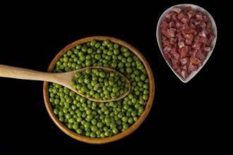 Wooden bowl with peas and white bowl with iberian ham isolated on black background