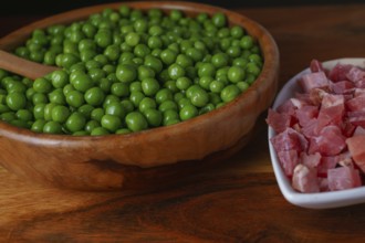 Wooden bowl with peas and white bowl with iberian ham isolated on black background