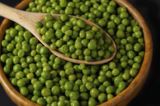 Wooden bowl with fresh peas and wooden spoon isolated on black background