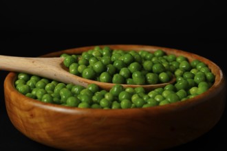 Wooden bowl with fresh peas and wooden spoon isolated on black background
