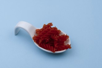 White ceramic spoon with red spiral macaroni and blue background
