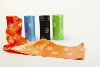 Orange dog poop bag unrolling with other colorful poop bags on a white background