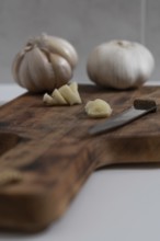 Whole and peeled garlic on wooden board and white background