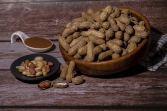 Peanuts in a wooden bowl and peeled peanuts on a plate with a spoonful of peanut butter