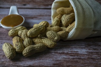 Peanuts in a raffia sack with a spoonful of peanut butter on a wooden bottom