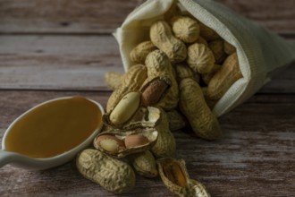 Peanuts in a raffia sack with a spoonful of peanut butter on a wooden bottom