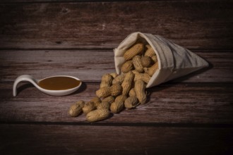 Peanuts in a raffia sack with a spoonful of peanut butter on a wooden bottom