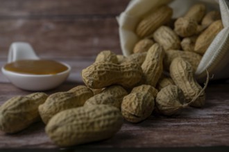 Peanuts in a raffia sack with a spoonful of peanut butter on a wooden bottom