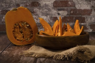 Cut pumpkin in wooden bowl on raffia cloth
