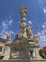 Baroque fountain with artistic sculptures under a slightly cloudy, blue sky Mödling Lower Austria