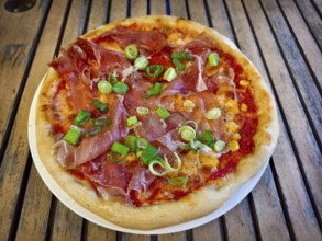 Pizza with ham and spring onions served on a table. Hearty and fresh with an Italian flavour