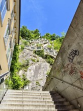 Modern stone staircase leads to a green rock under a clear sky, with graffiti stairs to the Graz