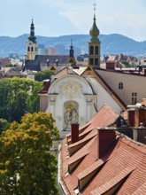 Panoramic view over the roofs of a historic city with church towers and mountains in the background