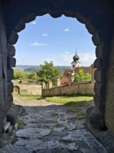 View through a stone Tor tor to a historic church and a landscape under a cloudy sky Riegersburg