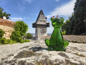 Green glass figure of a frog in front of historic clock tower
