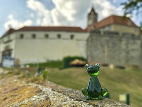 Glass figure of a frog king in front of a castle wall under a cloudy sky Riegersburg Styria Austria