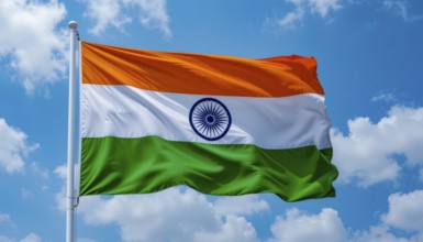 The Indian flag flutters against a bright blue sky dotted with puffy white clouds. A symbol of