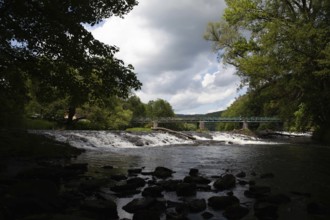 A forested stretch of river with a bridge and waterfall under a cloudy sky Hardegg Weinviertel