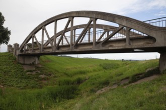 A concrete arch of the bridge stretches across a green meadow under a clear sky Perschling Flood