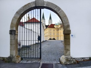 View through a Tor tor to a cobbled courtyard and church towers of a historic building,