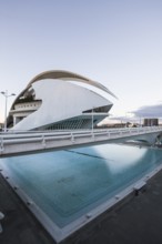 Modern building with curved design next to a reflecting pool at dusk Opera