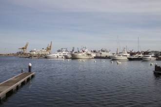 View of a busy harbour with yachts and industrial cranes in the background