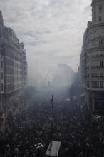 A large crowd gathers in a smoky city street MascletÃ¡ de Fallas