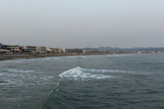 Houses on the seafront and surfers in the surf at dusk on the beach in Kamakura, Kanagawa