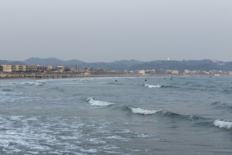 Houses on the seafront and surfers in the surf at dusk on the beach in Kamakura, Kanagawa