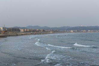 Houses on the seafront and surfers in the surf at dusk on the beach in Kamakura, Kanagawa