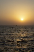 Background image, setting sun with silhouette of ship and land, water surface in evening light,